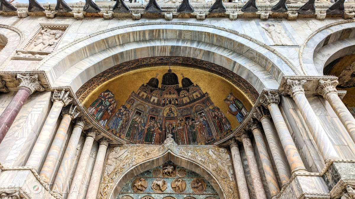 The oldest mosaic on the main façade is the one at the far left. Above, in the loggia, the four horses can be seen, and below the medallion of Jesus, the sarcophagus with the body of St. Mark is depicted.