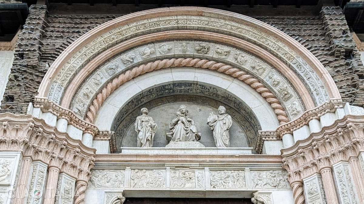 The statues above the portal depict St. Ambrose, the Virgin Mary, and St. Petronius. Below them, five bas-reliefs portray scenes from the New Testament.