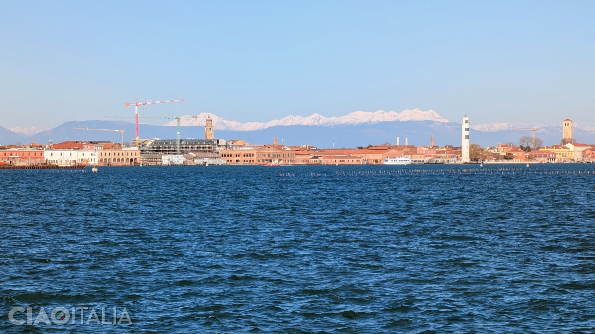 Beyond Murano island, the snow-covered summits of the Dolomites come into view.